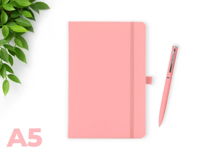 Wilson Pastel Pink A5 notebook with elastic closure and matching pen on a white background, with green leaves in the corner