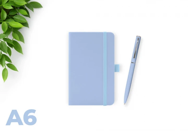 Wilson Pastel blue A6 notebook with elastic closure and matching pen on a white background, with green leaves in the corner